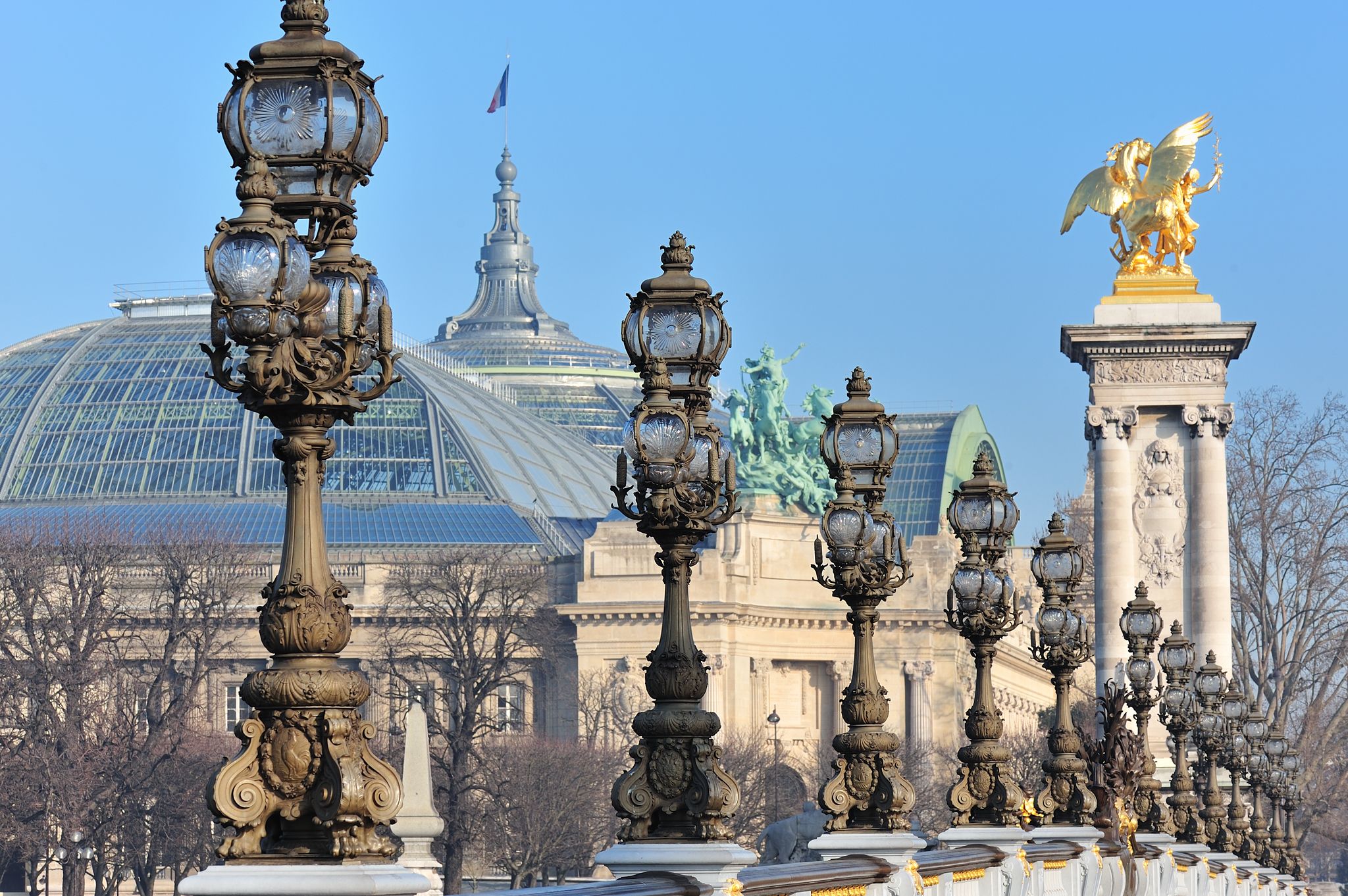 Photograph of a grand historic exhibition building façade with large arched windows and sculpted stonework, showing the iconic architecture of the Grand Palais in Paris. A monumental cultural venue with a sweeping glass‑roofed nave and ornate Beaux‑Arts details.