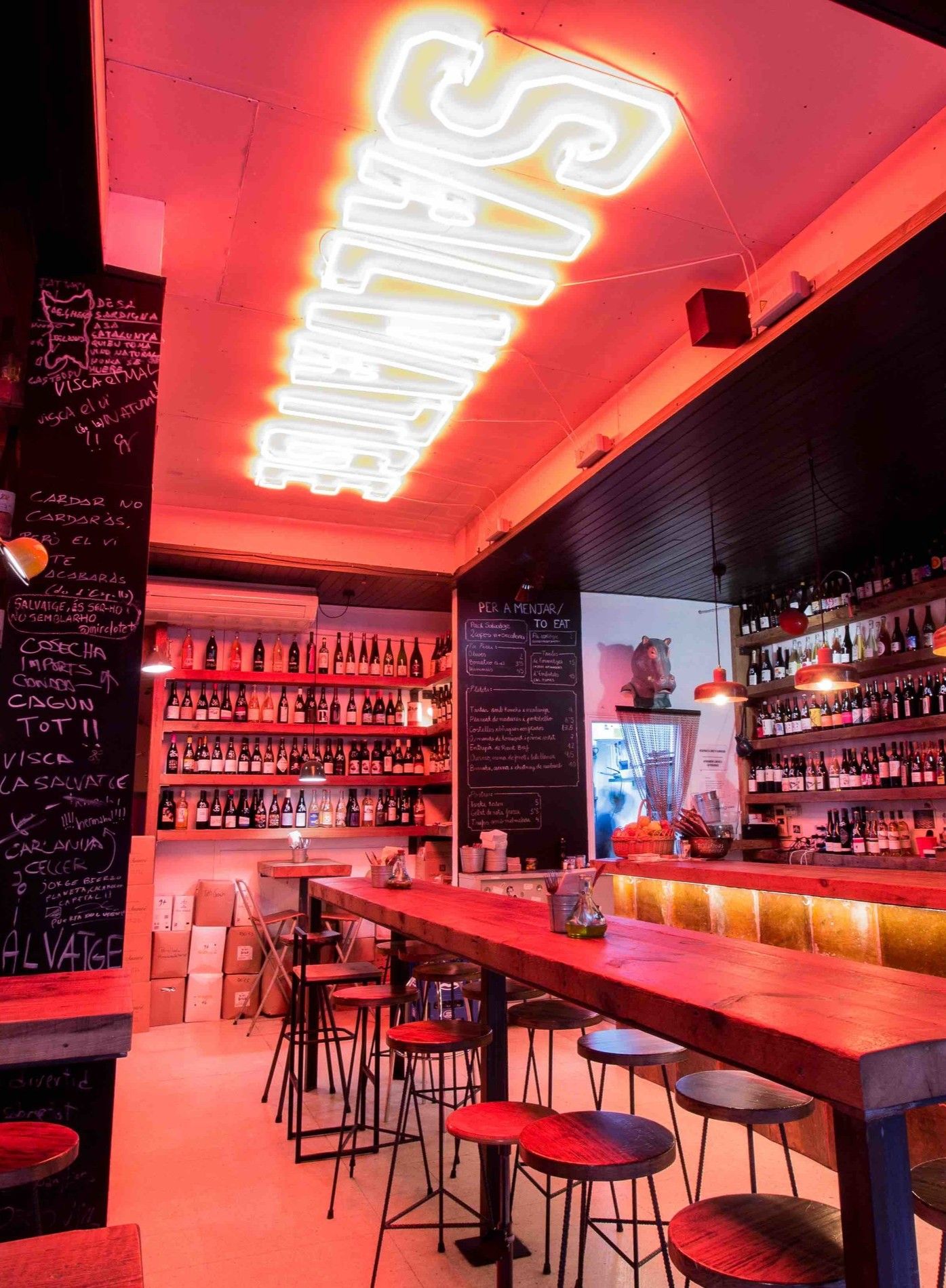 Interior of Bar Salvatge with red neon lighting, high tables, bar seating, and shelves stocked with bottles.