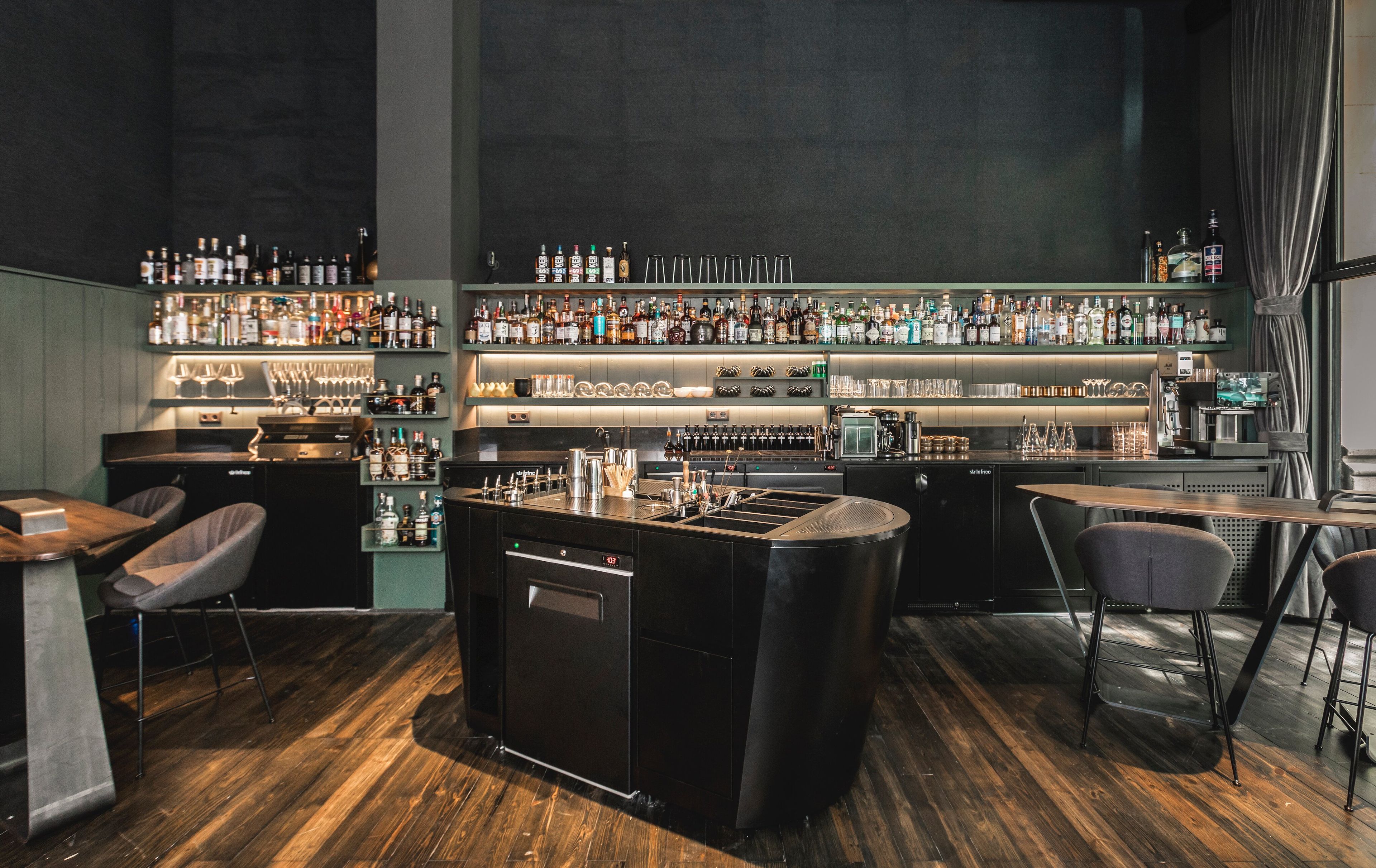 Sips Drinkery House cocktail bar interior with bottle-lined shelves, contemporary seating, and elegant ambient lighting.